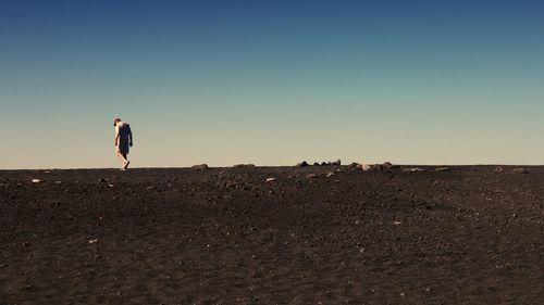 Rear view of woman walking on beach against clear sky during sunset