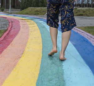 Female legs close up on barefoot on wet asphalt drawn rainbow walking path after rain among puddles