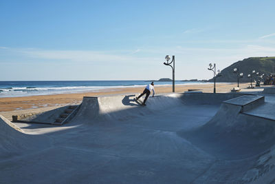 Unrecognizable teen boy riding skateboard in skate park on sunny day on seashore