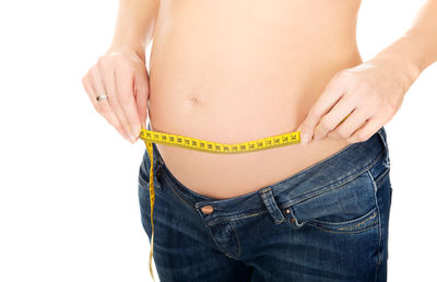 Midsection of woman measuring belly while standing against black background