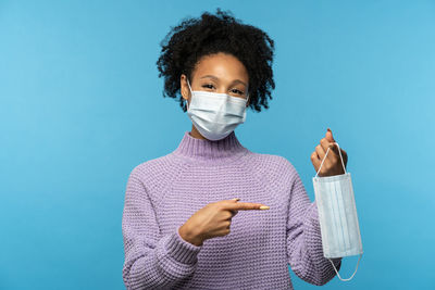 Portrait of young woman wearing mask against blue background