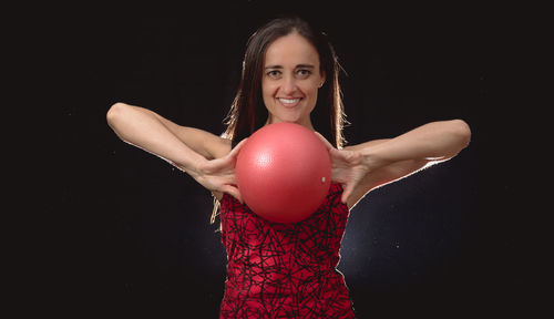 Portrait of mid adult woman holding fitness ball against black background