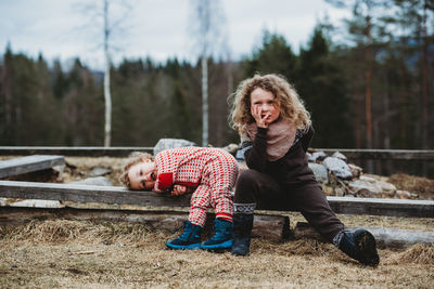 Boy and girl sitting on wooden log bored in the forest in winter