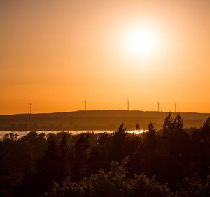 Silhouette wind turbines on field against sky during sunset