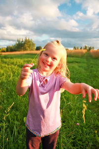 Portrait of smiling young woman standing on field against sky