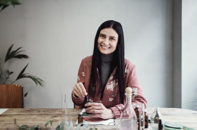 Portrait of smiling female entrepreneur preparing perfume at table in workshop