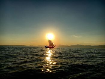 Silhouette boat sailing on sea against cloudy sky during sunset