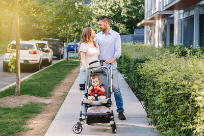 Urban life with kids children. caucasian mother and father walking with baby daughter in stroller. 