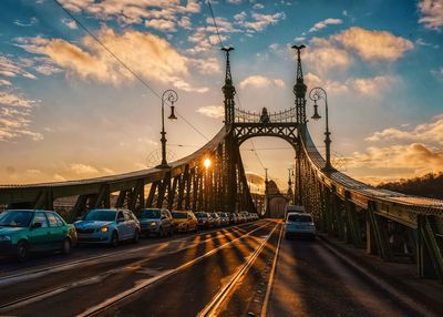 Cars on bridge in city against sky during sunset