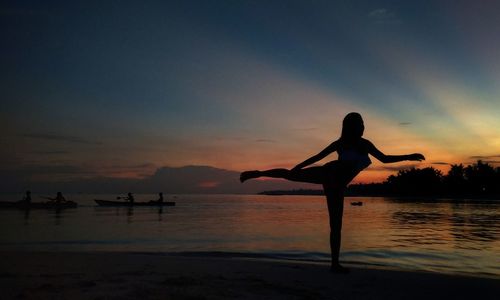 Silhouette woman exercising at beach during sunset