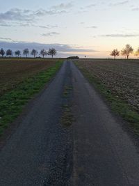 Empty road amidst field against sky during sunset