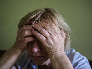 Sad woman with head in hands against green wall at home