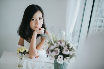 Portrait of woman sitting by flowers at home