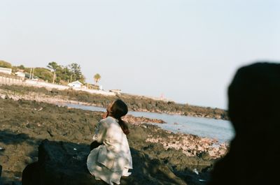 Rear view of woman praying at sea shore against clear sky