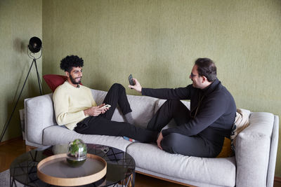 Gay couple relaxing on sofa at home and using phones