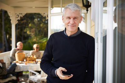 Portrait of smiling mature man standing on porch with friends in background