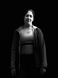 Portrait of teenage girl standing against black background