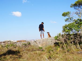 Low angle view of man standing with dog against sky