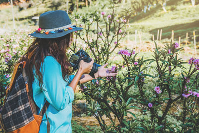 Side view of young woman photographing flowers from camera on land