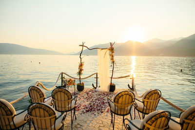 Chairs and table by sea against sky during sunset