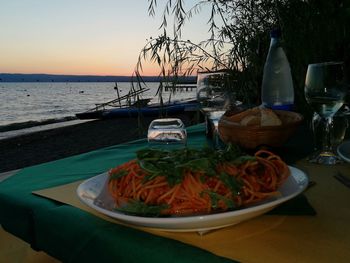 Close-up of food on table against sea during sunset