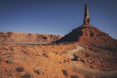 An orange car is driving through the valley of gods, utah