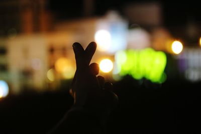 Silhouette hand against illuminated light at night