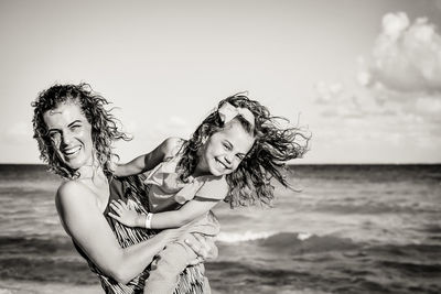 Portrait of young woman with arms raised on beach against sky