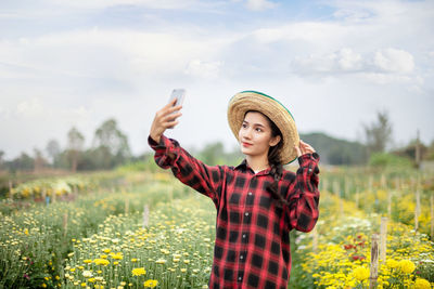 Young woman using mobile phone on field against sky