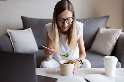 Young woman using phone while sitting on sofa at home