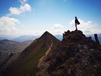 Side view of woman standing on cliff against sky