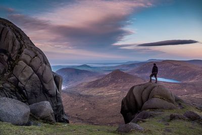 Full length of man standing on rock against cloudy sky at dusk