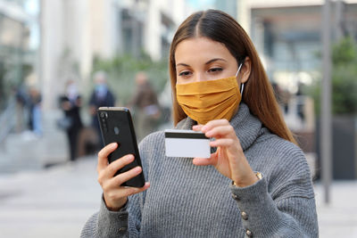 Portrait of young woman using mobile phone in city