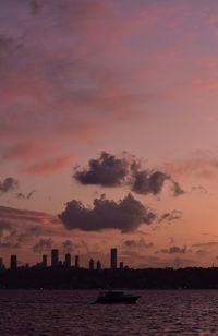 Silhouette buildings by sea against sky at sunset