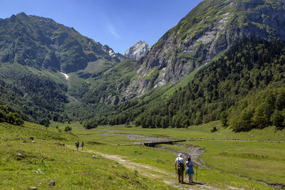 Rear view of people walking on field against mountains