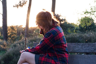 Side view of woman sitting on bench at sunset