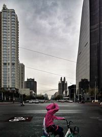 Rear view of woman riding motorcycle on road against buildings