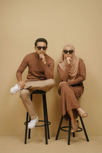 Portrait of young woman and man wearing sunglasses while sitting on clean background asian hijab cou