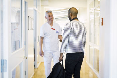 Smiling healthcare worker looking at male patient during visit in hospital corridor