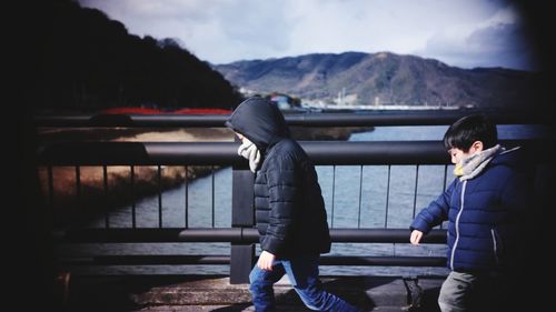 Side view of boys wearing warm clothing walking on bridge over river