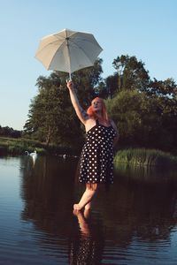 Redhead woman holding umbrella in lake against sky