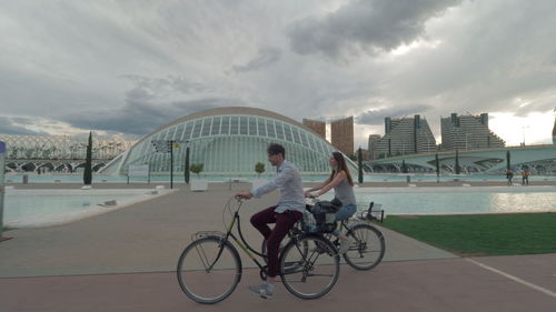 Man riding bicycle on bridge in city against sky