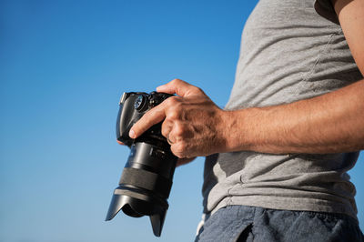 Midsection of man holding camera against clear blue sky