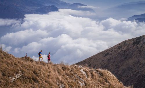 Side view of friends walking on mountain against cloudy sky