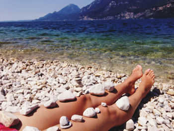 Low section of woman relaxing on pebbles at beach
