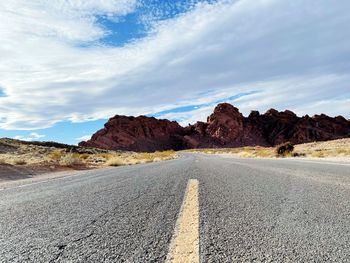 Empty road by mountains against sky