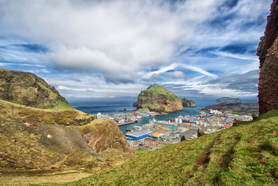 Buildings by sea and rock formations against cloudy sky