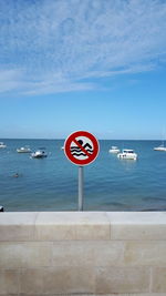 Information sign by sea against sky