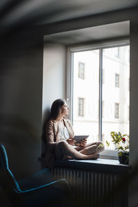 Young businesswoman sitting with tablet pc on window sill