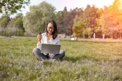 Young woman using laptop while sitting on field